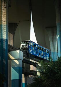 Blue monorail traversing beneath a large urban bridge during the day.