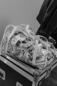 Black and white image of a clear bag packed with US dollar bills on a trunk.