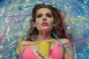 Portrait of woman in pink bikini surrounded by plastic waste highlighting environmental pollution.