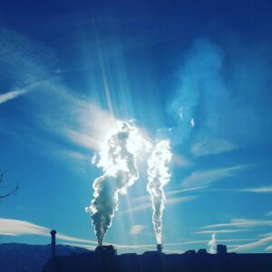 Silhouette of an industrial plant with steam emissions in a bright, clear sky.